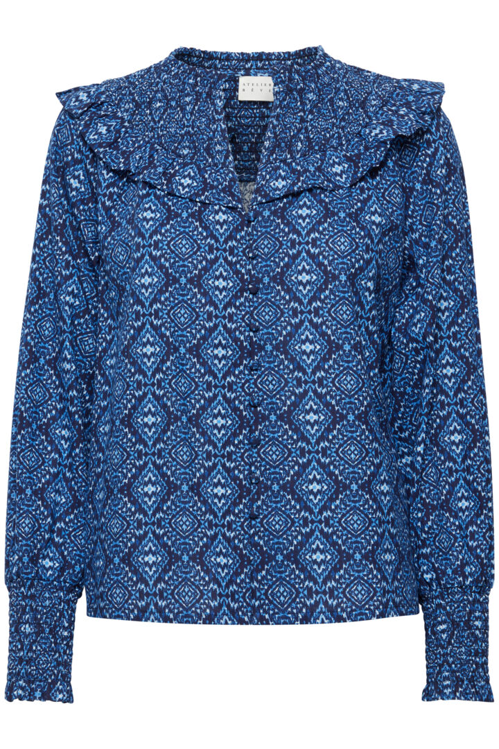 A stunning Ikat print shirt from Scandi brand Atelier Reve. The detail on this piece is incredibly feminine. A notch neck with shirring at the shoulders and a beautiful frill that goes around to the back. Long sleeves with a deep shirred cuff . This piece buttons form the neck to the hem with fabric covered buttons.