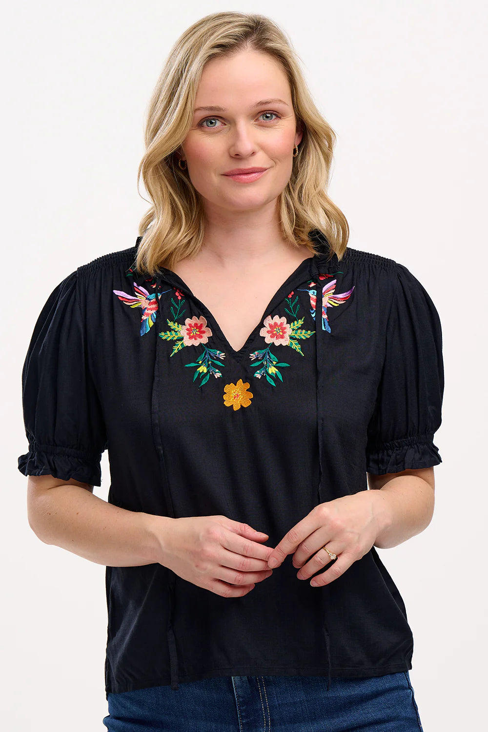 A simple Summer staple from SUGARHILL the new Angelique Blouse is perfect for work or weekend. The relaxed fit Angelique features shirring on the shoulders, short sleeves with shirred frill cuffs, a frill collar with ties and a flattering V-neckline. Featuring delicate floral embroidery around the neck line.
