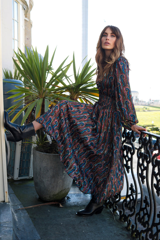 The Ballad dress from British brand Traffic People is a beautiful occasion piece. This stunning dress has a V neck with frill detail and buttons to fasten. The waist is elasticated for a flattering shape. The skirt is full and colourful. The full sleeves have an elasticated cuff. The fit is very neat. The fabric is quite sheer and would need a slip.