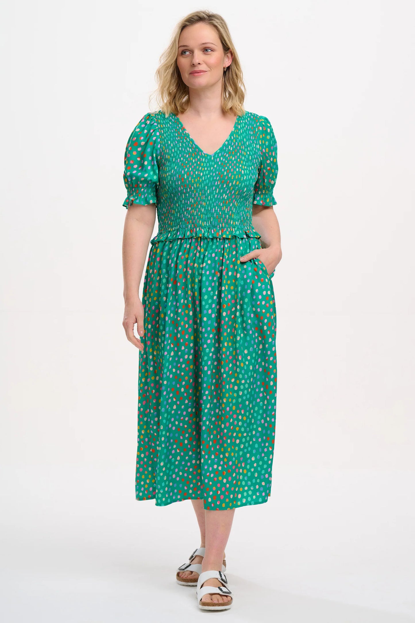 Introducing the Bettina from SUGARHILL. This perfect-for-summer dress has a V-neck shirred bodice, a delicate waist frill and gathered shirred sleeves to add an extra cuff frill. Featuring our new Rainbow Pebbles print of muted rainbow spots on a green base.