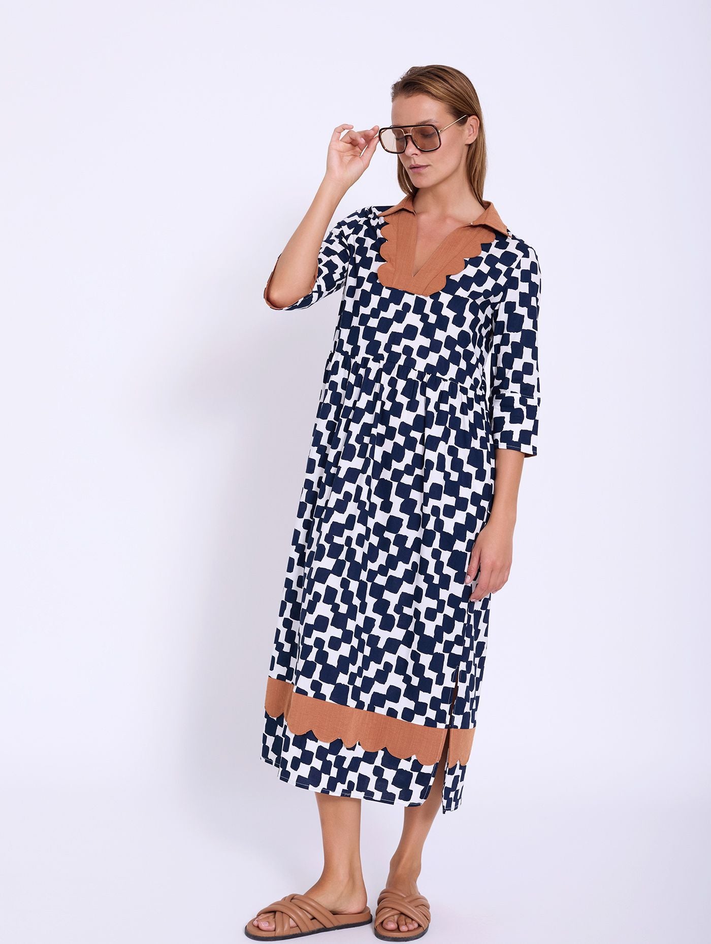 A beautiful summer dress from SKATIE in a bold navy and white print with accents of brick. A notch neck piece with contrast colour around the neckline. Elbow length sleeves with contrast lining. A gathered waist and side seam pockets. A midi length with a scalloped band around the bottom just above the hem. The fit is very neat. and there are side splits