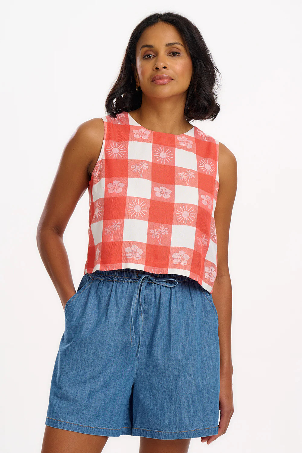 The NEW Bruna top from SUGARHILL offers a fresh take with its shorter, sleeveless design, complete with a round neckline and a stylish angular keyhole. The back neck features a convenient popper fastening for easy wear. Adorned with our new Tropical Gingham pattern in beautiful shades of coral and off-white, this piece is perfect for adding a touch of summer to your wardrobe.