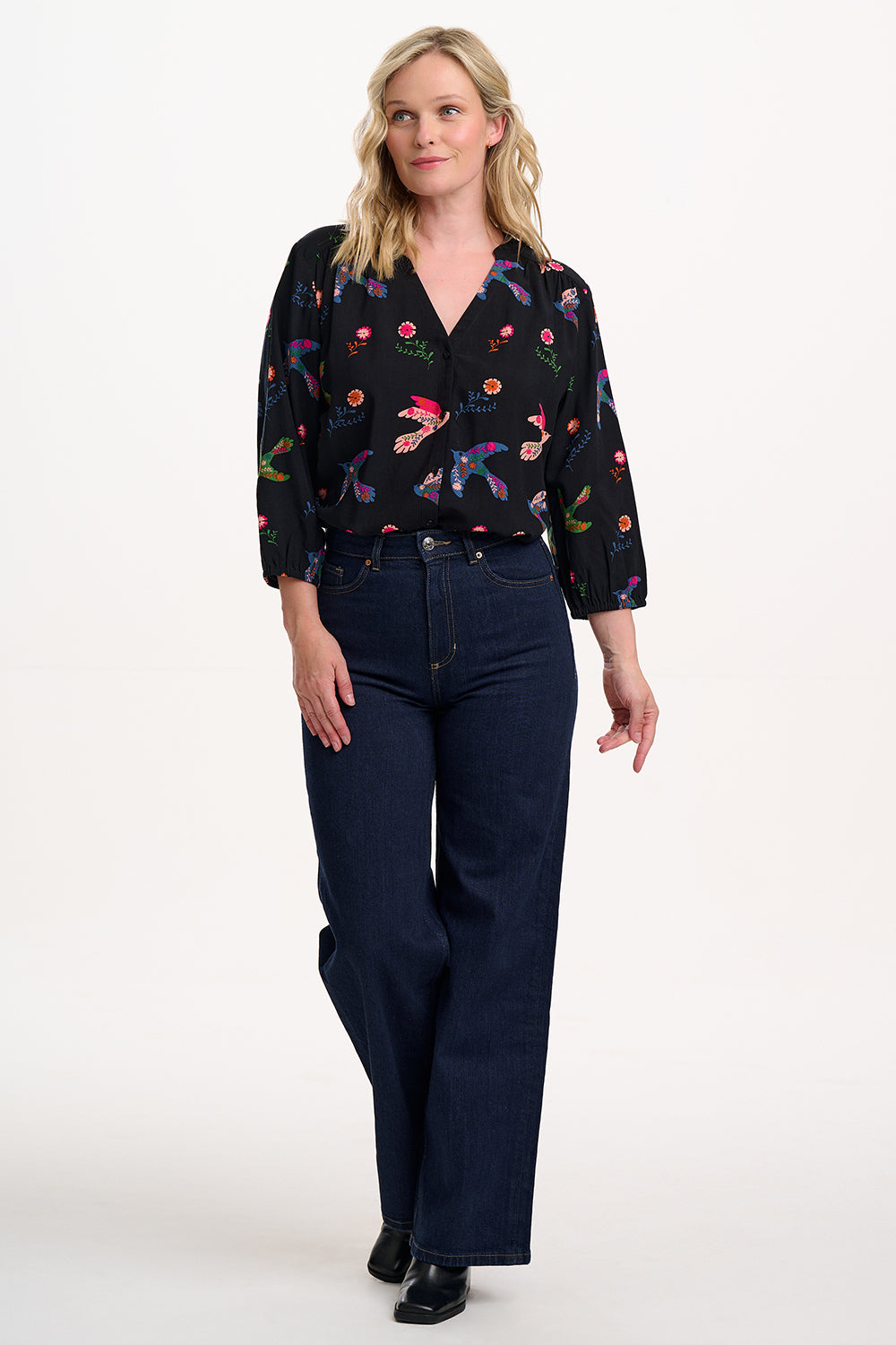 The Elkie Folk Bird Blouse form SUGARHILL blends boho charm with everyday wearability. This boxy-fit blouse features a collarless grandad neckline, gathered shoulder seams, and a functional button front. Subtle puff shoulders lead into full-length blouson sleeves finished with soft elasticated cuffs for a comfortable yet polished look. The standout design showcases vibrant folk-art birds and blooming florals scattered over a sleek black background, making it an eye-catching choice for both casual days and d