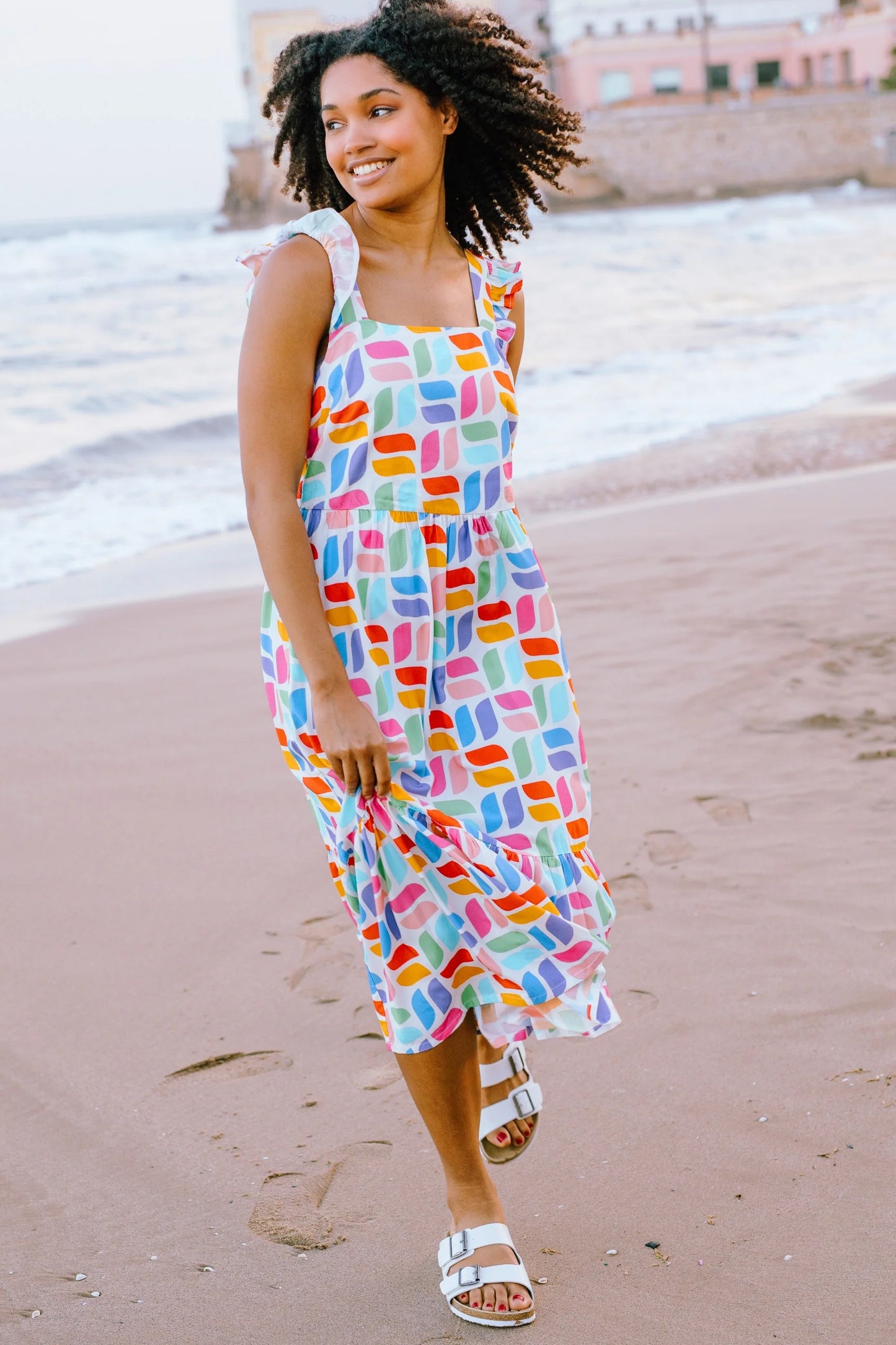 Estelle's shirred back panel and tiered skirt, complemented by a delicate frill shoulder, create a timeless summer piece from SUGARHILL. This design showcases our latest Curved Geometric print, featuring vibrant retro shapes against a soft off-white backdrop.