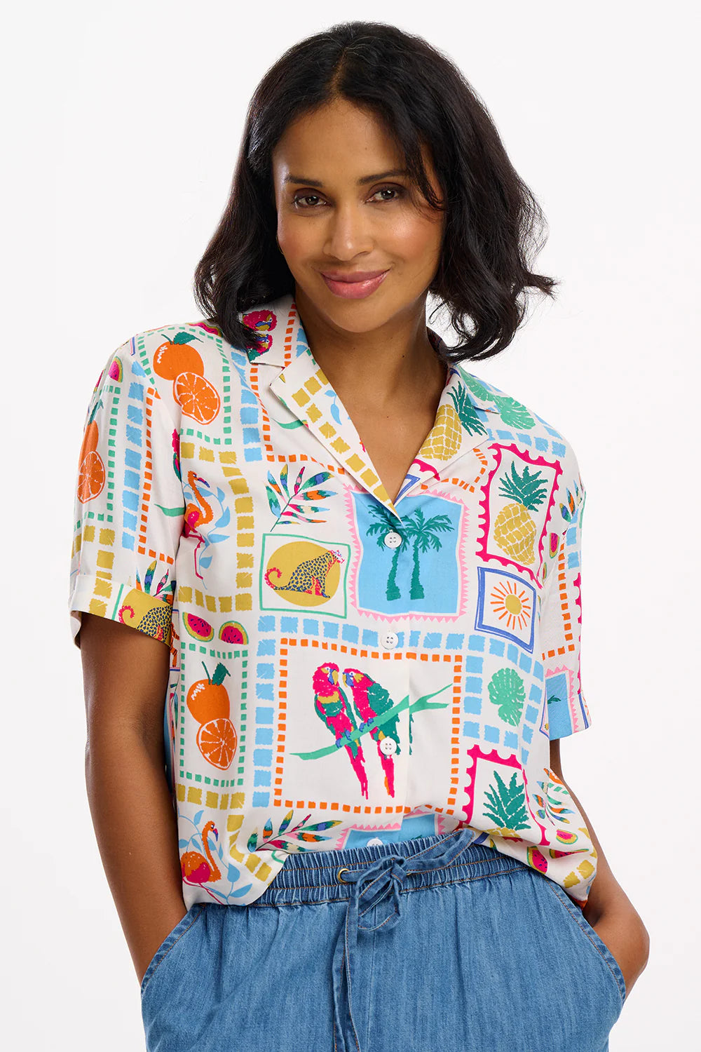 An updated twist on our popular Hatty Shirt by SUGARHILL, the Odele is cropped to fall above the hip. This short-sleeve shirt has the addition of a revere lapel collar, with functional buttoned front and turned back cuffs. Featuring our new Jungle Tile print of colourful tropical collage style wildlife, fruit and plants on an off-white base.