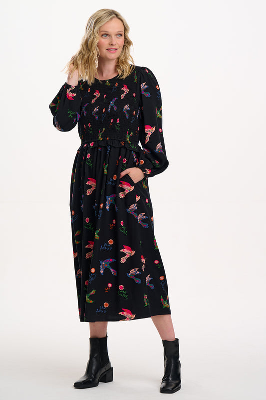 The Darcie Dress from SUGARHILL is here to brighten your day – and your wardrobe. Covered in vibrant folk-art birds and blooming florals, this midi is all about feel-good detail on a classic black base. It features a beautifully shirred bodice, long sleeves with gentle volume, and a flattering gathered skirt with – yes – pockets. A delicate keyhole fastening at the back adds a subtle finish. Dress it up with boots or down with trainers – Darcie’s an easy win for every occasion.