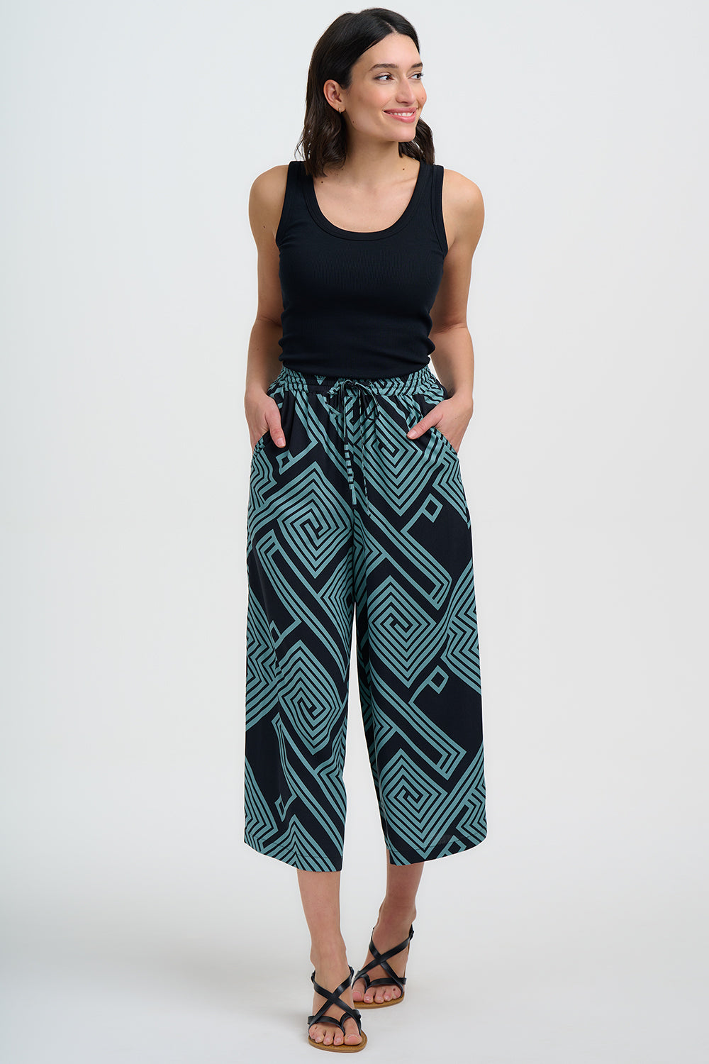 Step into summer with the Ameera Cropped Wide-Leg Trousers from SUGARHILL, the perfect blend of comfort and vibrant style. Cut to a cropped length that falls just above the ankle, they feature a relaxed wide-leg shape, an elasticated waistband with an adjustable drawstring tie, and handy side pockets for everyday ease. Featuring our new teal geometric spirals and diamonds design, creating a bold, maze-like pattern on a black background. Pair with sandals and a tee for daytime chic or elevate with wedges for