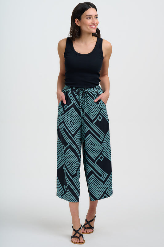 Step into summer with the Ameera Cropped Wide-Leg Trousers from SUGARHILL, the perfect blend of comfort and vibrant style. Cut to a cropped length that falls just above the ankle, they feature a relaxed wide-leg shape, an elasticated waistband with an adjustable drawstring tie, and handy side pockets for everyday ease. Featuring our new teal geometric spirals and diamonds design, creating a bold, maze-like pattern on a black background. Pair with sandals and a tee for daytime chic or elevate with wedges for