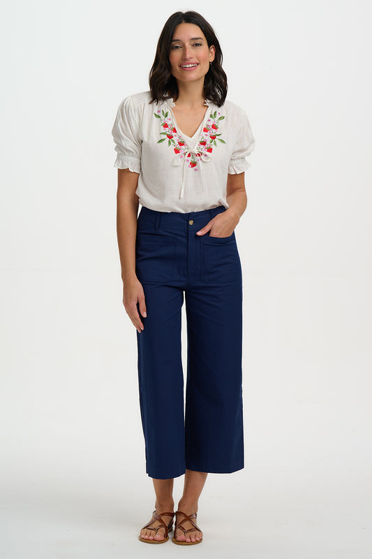 The Angelique Blouse is a versatile summer staple, perfect for both workdays and weekends. Crafted from lightweight fabric, it features delicate shirring at the shoulders, short sleeves with shirred frill cuffs, and a pretty frill collar with tie detailing. The flattering V-neckline is adorned with intricate floral embroidery in vibrant hues, adding a feminine touch to the elegant black white. Effortlessly stylish, this blouse pairs beautifully with denim for casual days or tailored trousers for a polished 