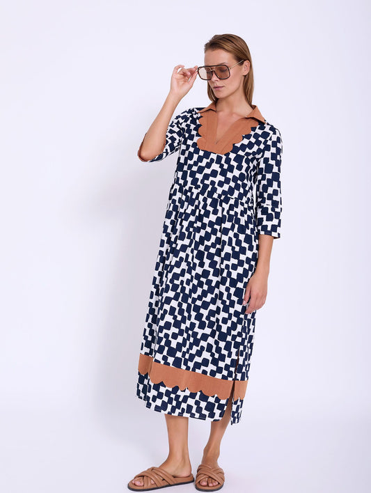 A beautiful summer dress from SKATIE in a bold navy and white print with accents of brick. A notch neck piece with contrast colour around the neckline. Elbow length sleeves with contrast lining. A gathered waist and side seam pockets. A midi length with a scalloped band around the bottom just above the hem. The fit is very neat. and there are side splits