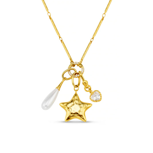 The Mixed Charm Long Cluster Necklace pairs an elongated bar-link chain with a distinctive trio of charms. A bold molten-textured star, a delicate teardrop pearl, and a sparkling heart-shaped crystal. Each charm is connected to a crystal-accented ring, forming a striking clustered arrangement that catches the light beautifully.