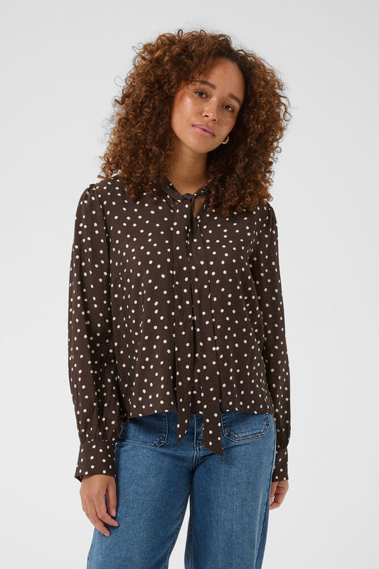 Polka dot blouse from KAFFE featuring a relaxed straight fit, statement tie neckline, and voluminous long sleeves with buttoned cuffs. Subtle gathers add movement. A great piece for tonal dressing this Autumn.