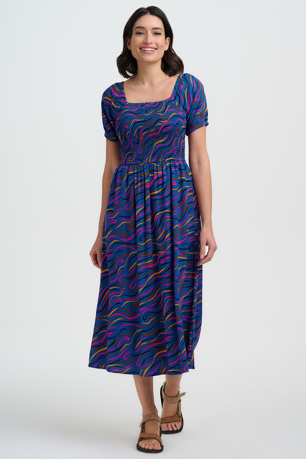 The Jolene Midi Dress is an effortlessly stylish choice for everyday wear. Designed with a square neckline, short puff sleeves, and a shirred elasticated bust for a flattering and comfortable fit. The dress features a high waist and a full midi skirt with practical side pockets. Showcasing the vibrant tiger-stripe waves in orange, pink, and black that flow across a deep 