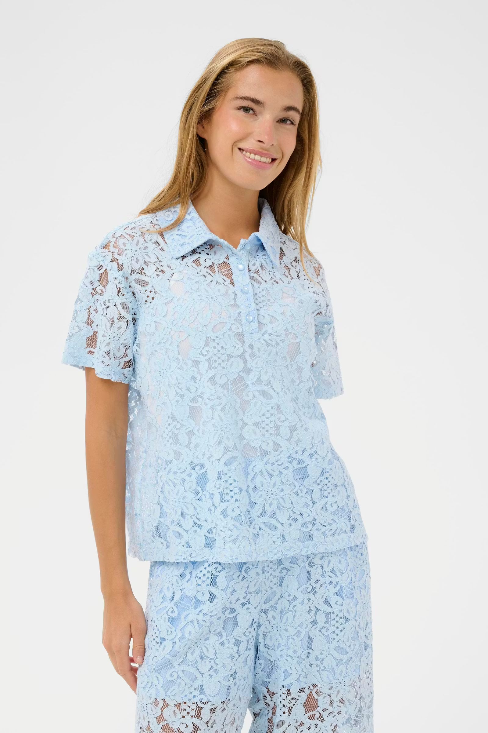 Lace shirt from Scandi brand KAFFE featuring a classic polo collar and short sleeves. Straight fit with a button placket at the front. The allover floral lace texture creates a semi-sheer appearance throughout. Hem finishes at hip length. The fit is true to size.