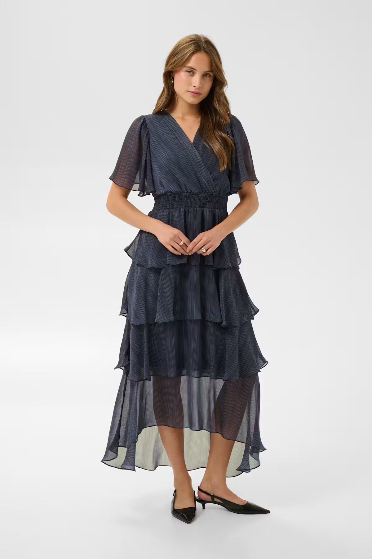 This dress from KAFFE features a layered silhouette with tiered ruffles and a fitted, elasticated waist. The V-neckline, flutter short sleeves, and ankle-grazing length enhance the fluid drape and contemporary look, while the semi-sheer textured surface and wrap-effect bodice add definition and light movement.