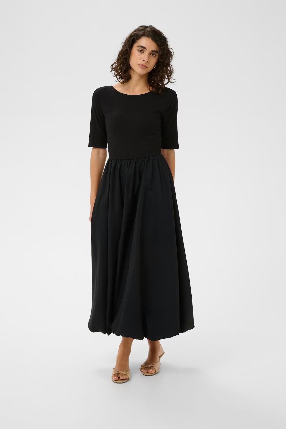 Maxi dress from KAFFE with fitted bodice, scoop neckline, and elbow-length sleeves. Voluminous gathered skirt with unique rounded hem creates striking silhouette. Clean, modern lines for a confident statement look.