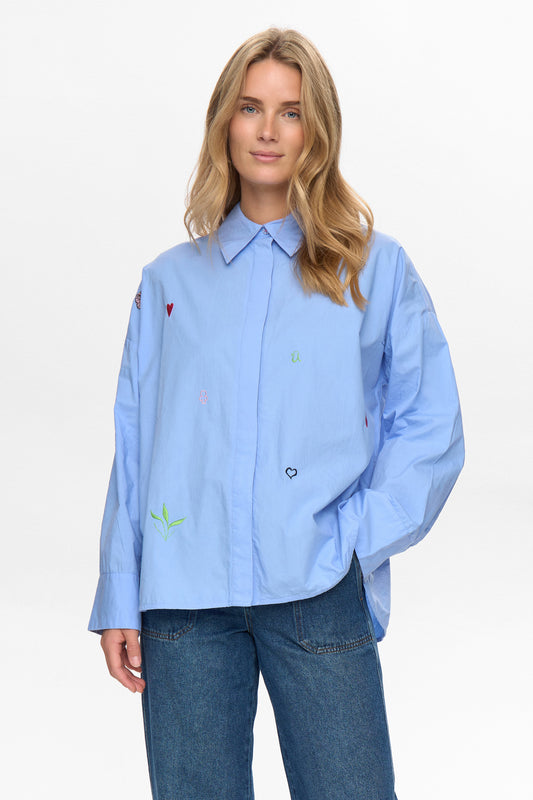 A classic but very oversized shirt with a standard collar and button front from NUMPH. Long sleeves with a wide cuff with two buttons to allow a different fit . The cuff is lined in a striped fabric so can be worn turned back. There are embroidered embellishments on the front and the words "To forever ever land" embroidered at the hem. The fit is very oversized.