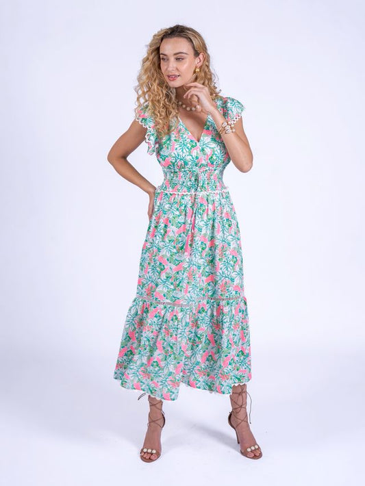 The New Day Originals Misha Dress is a playful and feminine piece in soft poplin cotton, featuring a whimsical pink parrot print. It has a smocked waist, a V-neckline with cap sleeves, and a tiered A-line skirt that falls to mid-shin, finished with handmade red resin tassels for a charming, artisanal touch.