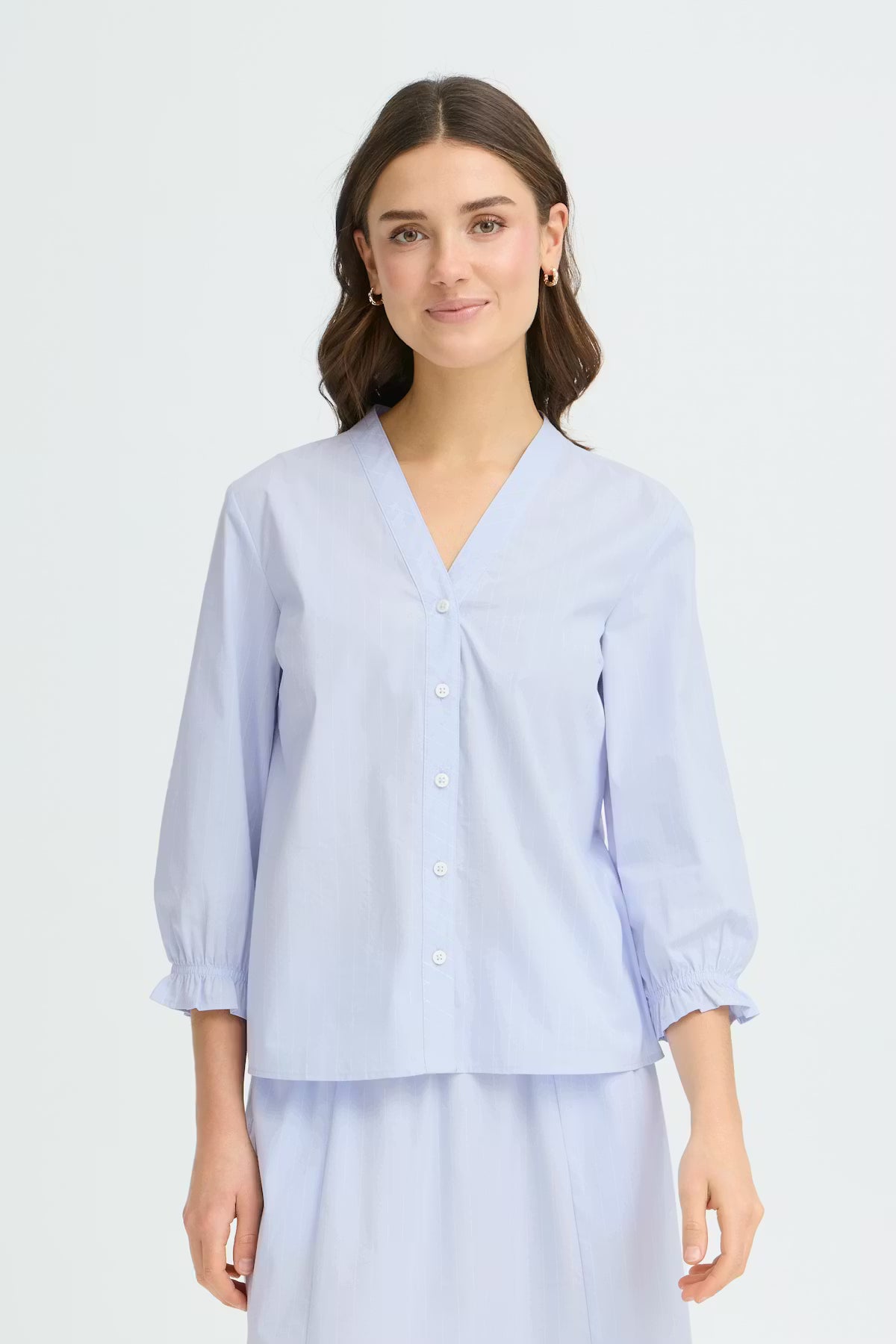 This button-up blouse from FRANSA features a subtle stripe look, a relaxed straight fit, a V-neckline, and three-quarter sleeves with gentle ruffle cuffs for effortless polish.